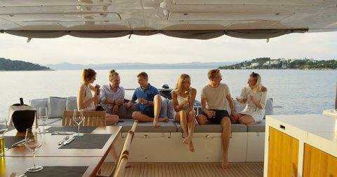 Group of Successful Young People Have Great Time in the Stern of a Yacht, They Drink Cocktails, Talk and Have Fun. In the Background Sea and Islands. Shot on RED Epic 4K UHD Camera.