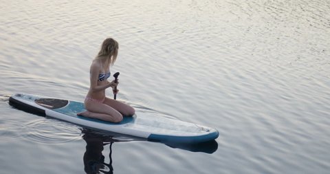 Fit Young Woman Sits on a Paddleboard Looking into the Sea. Shot on RED Epic 4K UHD Camera.