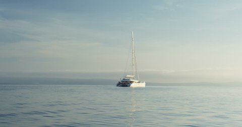 White Catamaran Yacht Sailing on a Beautiful Azure Sea with Land in the Background. Shot on RED Epic 4K UHD Camera.