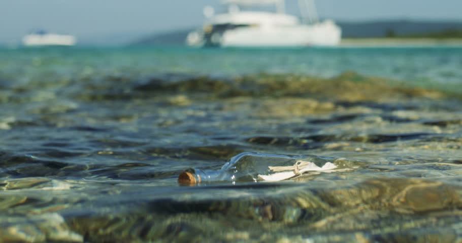 Close-up Shot of a Message in the Bottle, Drifting in Shallow Seas with White Yacht in the Background. Shot on RED Epic 4K UHD Camera.