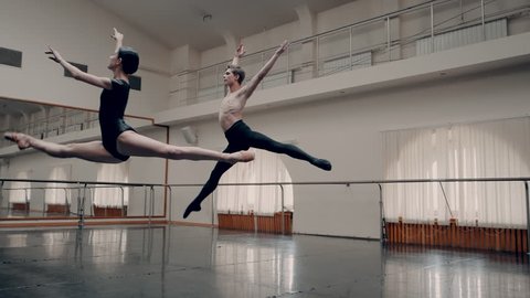 Young man practicing in classical ballet with young beautiful woman in black clothing in the gym or ballet hall. Couple jumping. Minimalism interior, sensual dance. Slow motion. adagio