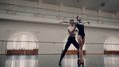Young man practicing in classical ballet with young beautiful woman in black tutu clothing in the gym. he carrying the girl on shoulders Minimalism interior, sensual dance. Slow motion