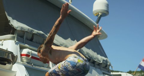 Slow Motion Shot Athletic Young Man Does Backflip into the Sea From Yacht's Swim Platform. Shot on RED Epic 4K UHD Camera.