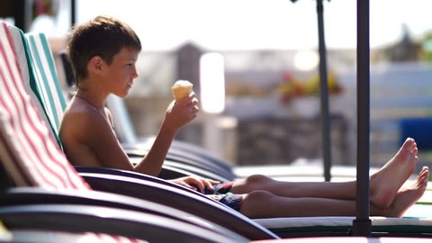 boy eating an ice cream on a lounger near the swimming pool in the hotel