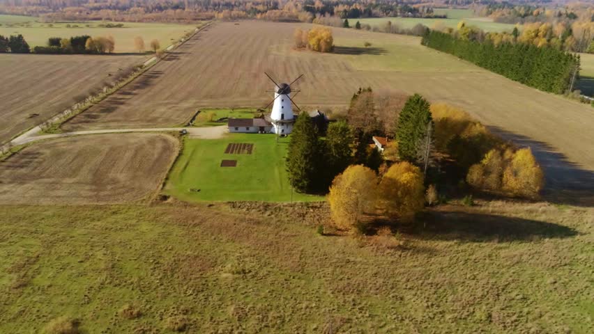 Aerial approach to a historic windmill between golden fields in autumn