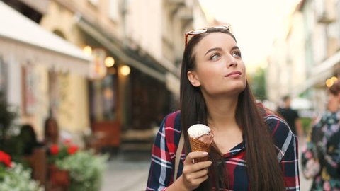 Close up shot of beautiful young woman walking the street and eating icecream. Woman traveling in the old city