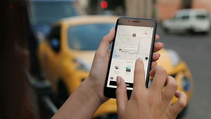 New york - july 20, 2017: uber application. woman ordering taxi on the  white smartphone via uber app. outdoors. blurred background. close up