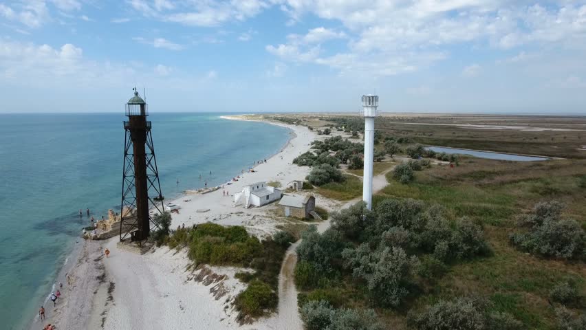 A gorgeous bird`s eye view of a white beacon and a black border tower on Dzharylhach island with wonderful seacoast covered with green wetland and sand in summer. The sky is full of white clouds
