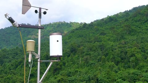 Meteorological weather station antenna with meteorology sensors, pale overcast cloudy sky and forest in background. Weather station for background.