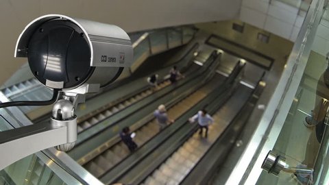 Closeup CCTV security camera operating with escalator system and people