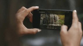 young woman takes a waterfall on a smartphone while traveling