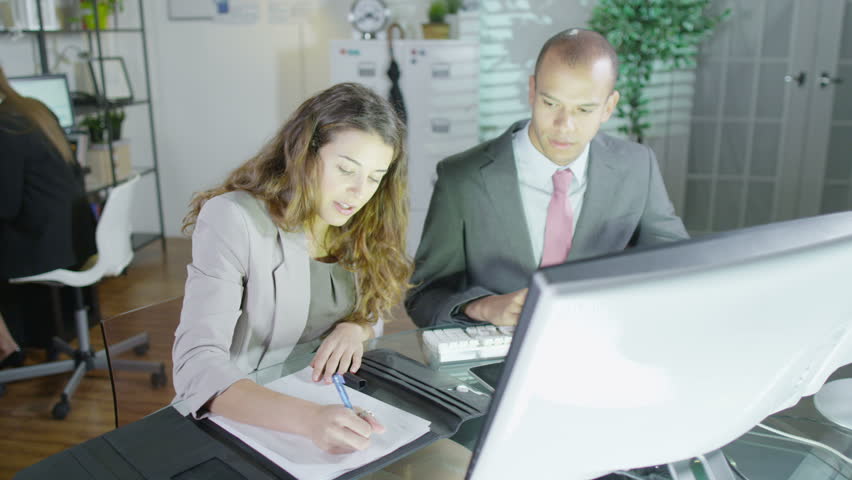 Office or security workers sitting and working together in front of their computers. Another worker can be seen in the background with a whole bank of computer monitors in front of her. Slow motion Royalty-Free Stock Footage #3220189
