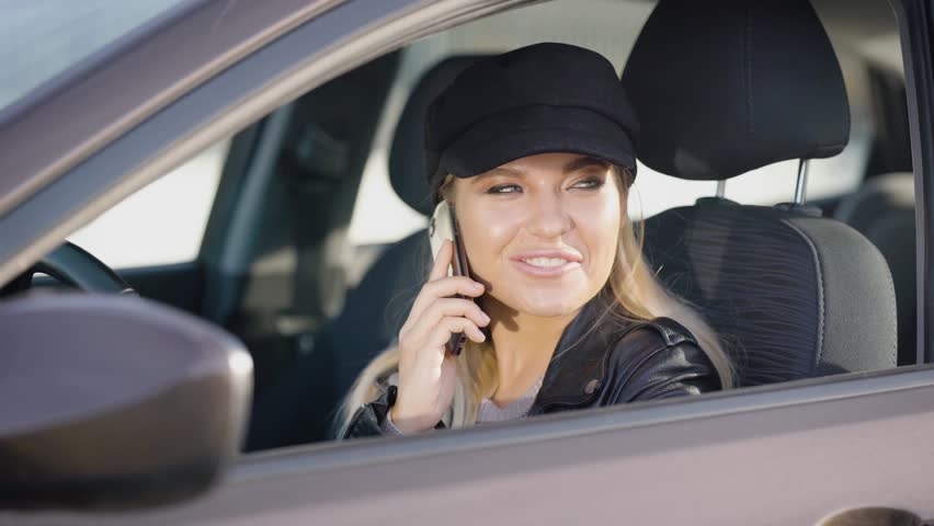 Stylish young model sitting in car and talking on phone happily