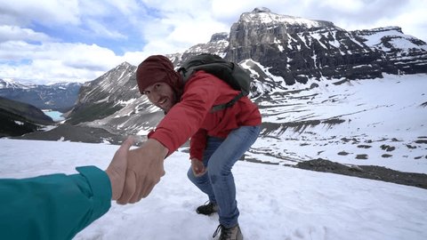 A helping hand from teammate on top of the mountain. Partner outstretches arm to reach the one of hiker going up to help him out. People exploration adventure concept 