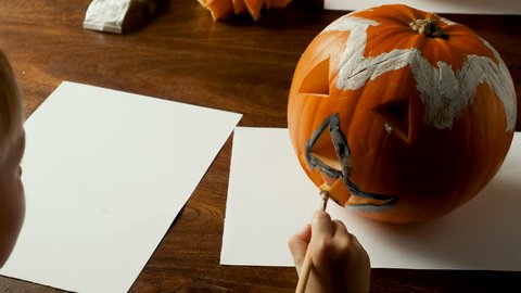 Young boy painting a pumpkin for Halloween on a table