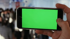 male hand horizontal keeping smart phone green screen chromakey closeup man people airport railway station blurred background checking schedule conversation video call online chat application trade