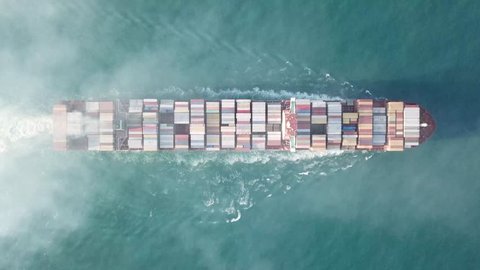 Early morning aerial top-down view of Mega large ULCV container ship sails on open water fully loaded with containers and cargo - 366m long 145K ton - smoke is coming from the chimney