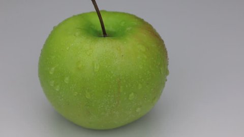 Rotation of a green apple in drops of dew on a white background.