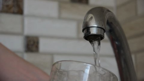 Hand Keeps A Glass. Pouring Water From A Metal Tap Into A Glass In The Kitchen.