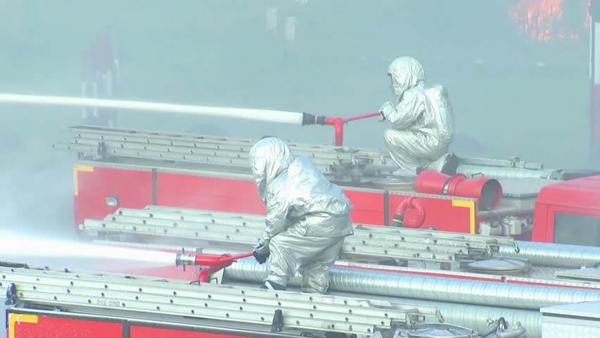Firefighters in fire-retardant and heat-reflecting suits extinguish the fire from a hose installed on cars. Elimination of fire and man-made disaster.