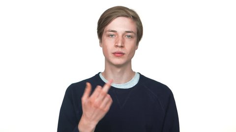 portrait of young male hipster suddenly appearing from bottom on camera with poker face showing fuck you sign over white background closeup copy space. Concept of emotions
