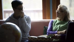 Camera pushing in on a mother and teenage son doing homeschool lessons in a relaxed environment with a globe of the earth in front. Clip goes from blurry to sharp on the student and