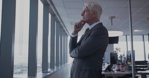 Side view shot of mature businessman standing in office and looking outside the window. Male entrepreneur standing in office and thinking.