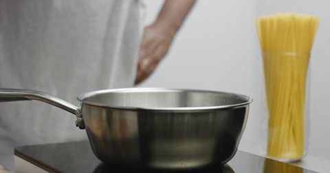 Chef in gray apron pours water to a large stainless steel pot and mixes with a wooden spatula on white background