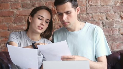 Young man and woman having problems with documents, confused couple looking through papers sitting at home with laptop, checking unpaid bills, worried about overdue debt, searching legal help online