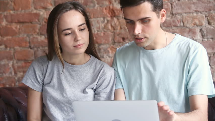 Young casual couple using laptop sitting on couch at home, choosing best sale offers, purchasing goods in online shop together, searching cheap travel tours, booking hotel abroad, comparing prices Royalty-Free Stock Footage #32239255