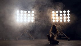 a young woman of pleasant appearance dances in the training hall in the lighting of searchlights in the background. a professional dance girl performs the set number in the style of lacquering and