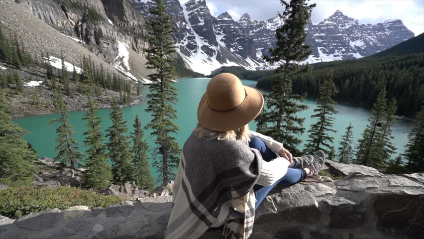 Young woman contemplating nature by the lakeshore; slow motion shot at Moraine lake in Banff national park, Canada