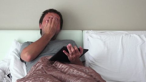 Using digital tablet for social network activities in bedroom, man with portable touchscreen computer device in bed.