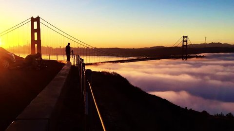 Morning time lapse of low fog traveling under the Golden Gate Bridge in San Francisco with photographers and an orange and yellow spectacular skyline