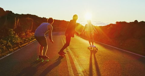 Skateboarders riding down hill into the sunset