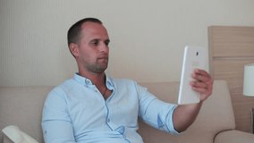 Man lying on the sofa using his digital tablet at home in the living room.