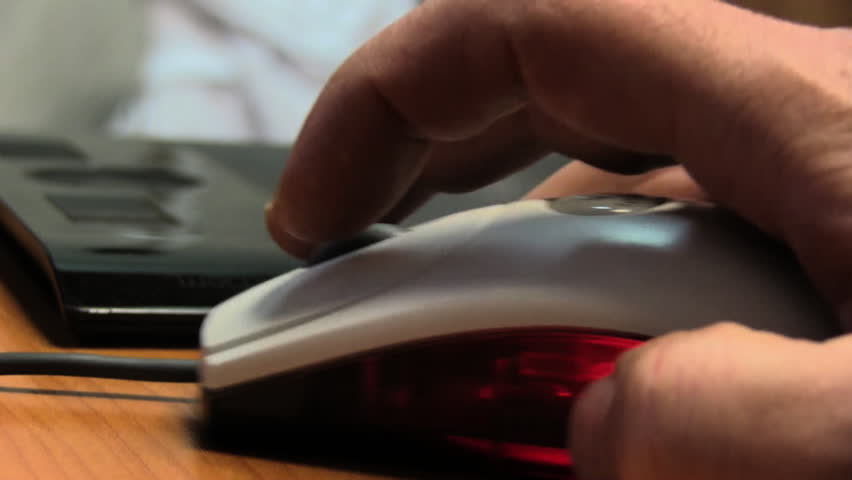 Hand of a man working at computer clicking on mouse on dark desktop