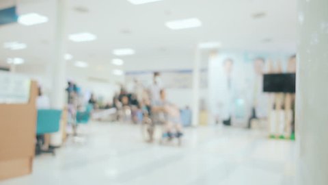 Locked shot and blurred with Scene inside the hospital, Someone has to push the wheelchair with patient and other people walk around the hall way