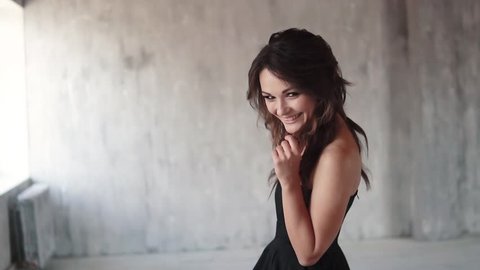 portrait of attractive girl in a black dress. young woman with evening make-up playfully smiling at the camera. slow motion