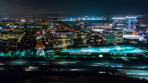 Aerial timelapse in motion (hyperlapse) at night along urban California city and interstate with cars, traffic and high-rise buildings below.