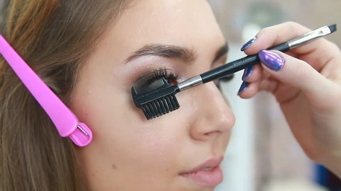 Professional make-up artist applying mascara on eyelashes of model in white room. Beauty, make up and fashion concept