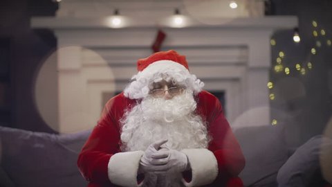 Pensive Santa Claus sitting on couch at Christmas eve. Santa Claus waiting Christmas night for congratulation children. Christmas vibes and New Year eve celebration