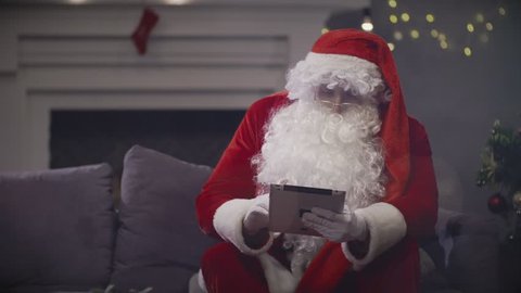 Santa Claus reading letters on tablet screen from children. Santa Claus using tablet for Christmas wishes and congratulation online. Christmas mood in holiday
