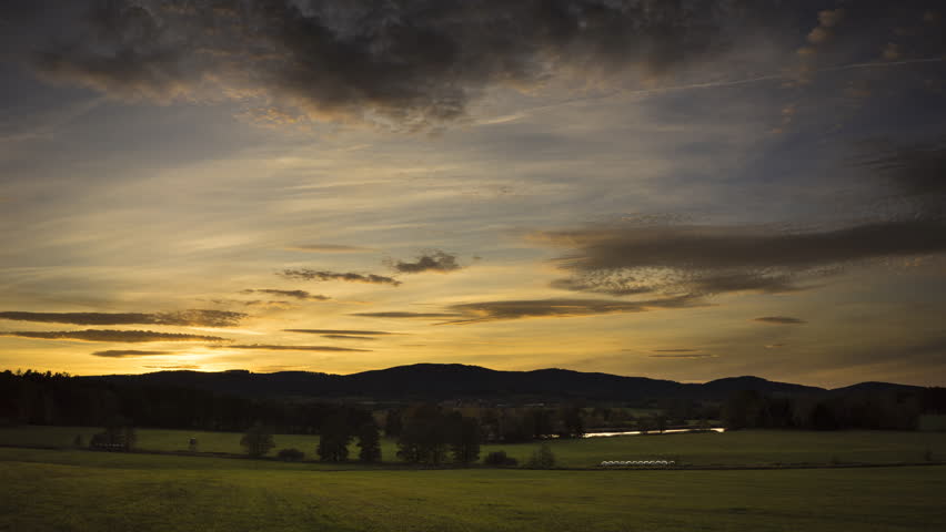 Green meadows and small hills under the gold and blue sunset with clouds. Timelapse video.