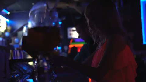 A lonely beautiful girl sits in a nightclub and drinks a cocktail.