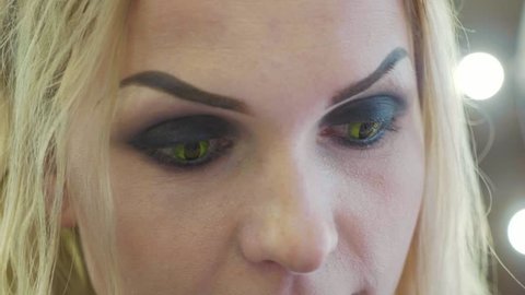 Close-up portrait of young pretty woman with halloween makeup at beauty salon. Face of lady with cat eyes contact lenses in slow motion.