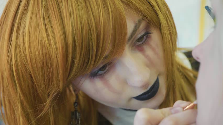 Beautiful girl artist with halloween makeup at work. Process applying halloween makeup on model