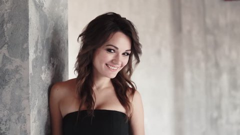 portrait of attractive girl in a black dress. young woman with evening make-up playfully smiling at the camera. girl with smoky eyes