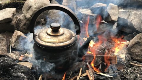 Kettle smoke flying ashes fire arms Boiling kettle fire log steam Camping Burning hiking camp woods nature wood trip authentic summer kitchen backpack axe tea pot boiling over open fire