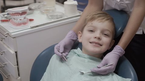 Portrait of smiling little boy shows thumb up in dentist chair
